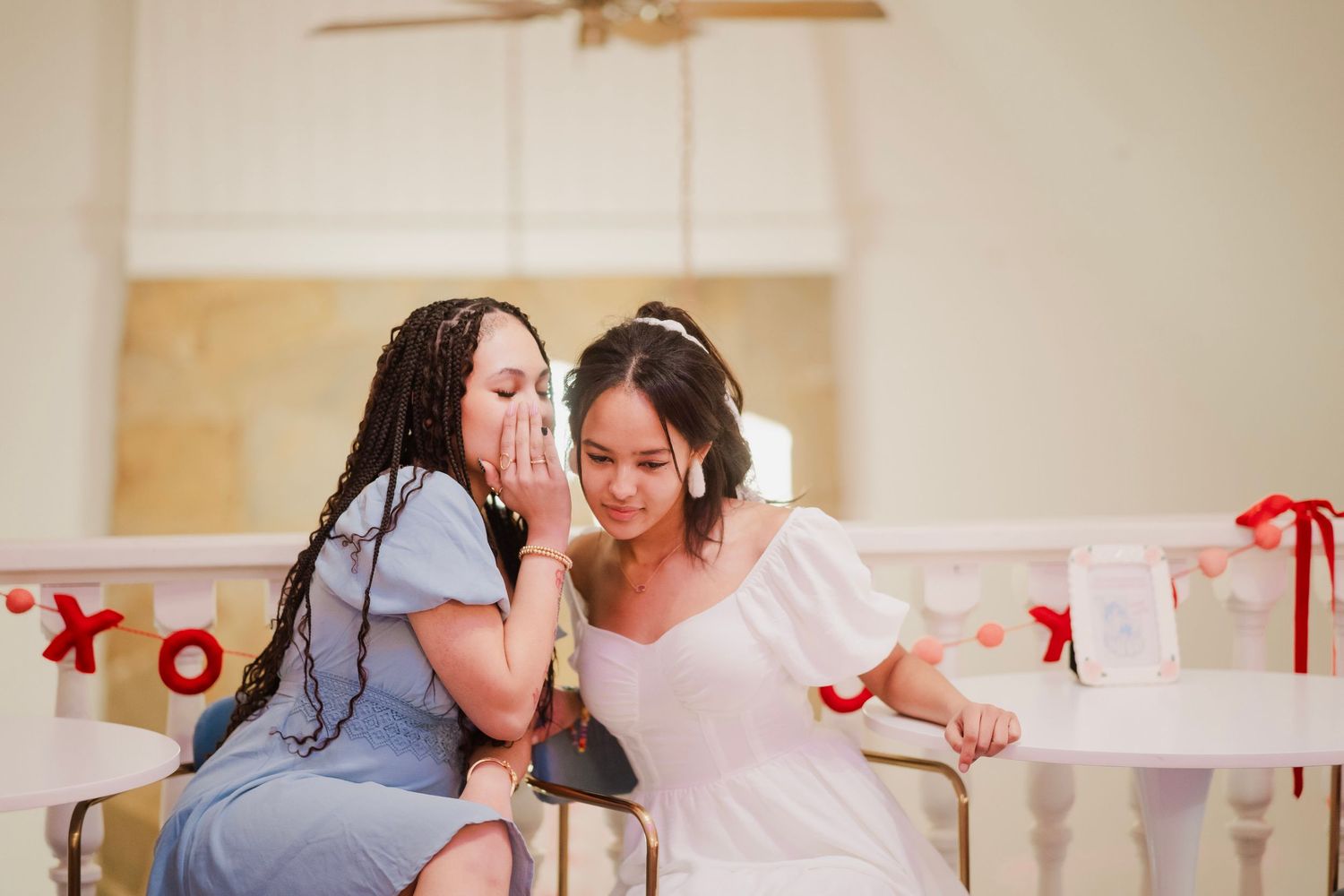 Two women share a secret whisper at a Valentine's Day decorated table indoors.