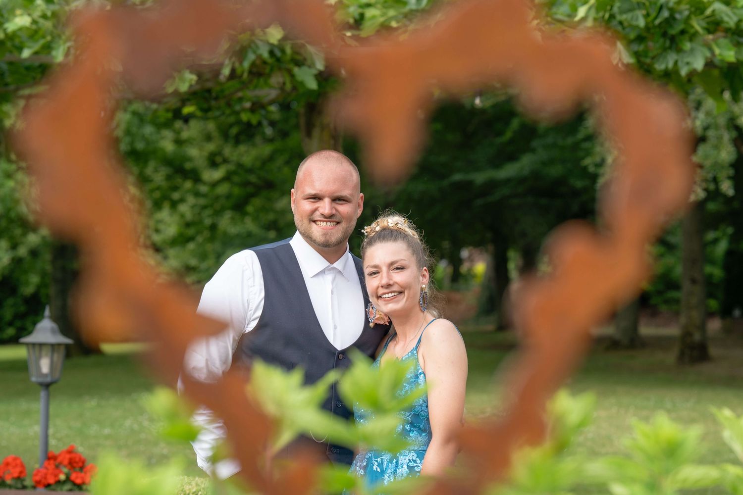 Wedding guests enjoying a candid moment in a lush green garden setting with red flowers in the foreground.