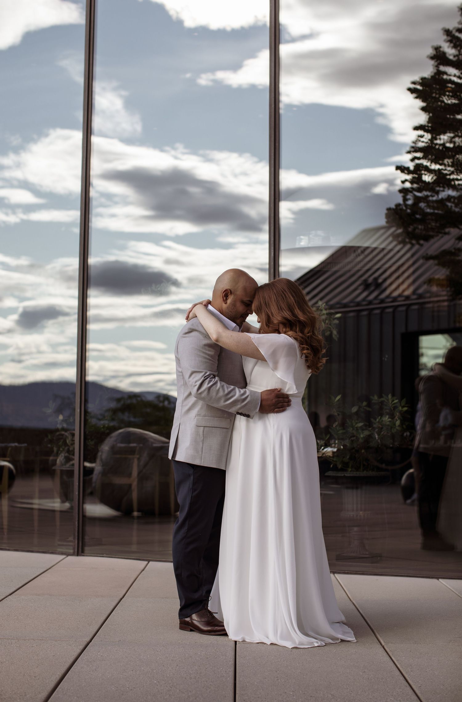 A couple shares their first dance as newlyweds on an outdoor terrace with dramatic cloudy skies in the background.