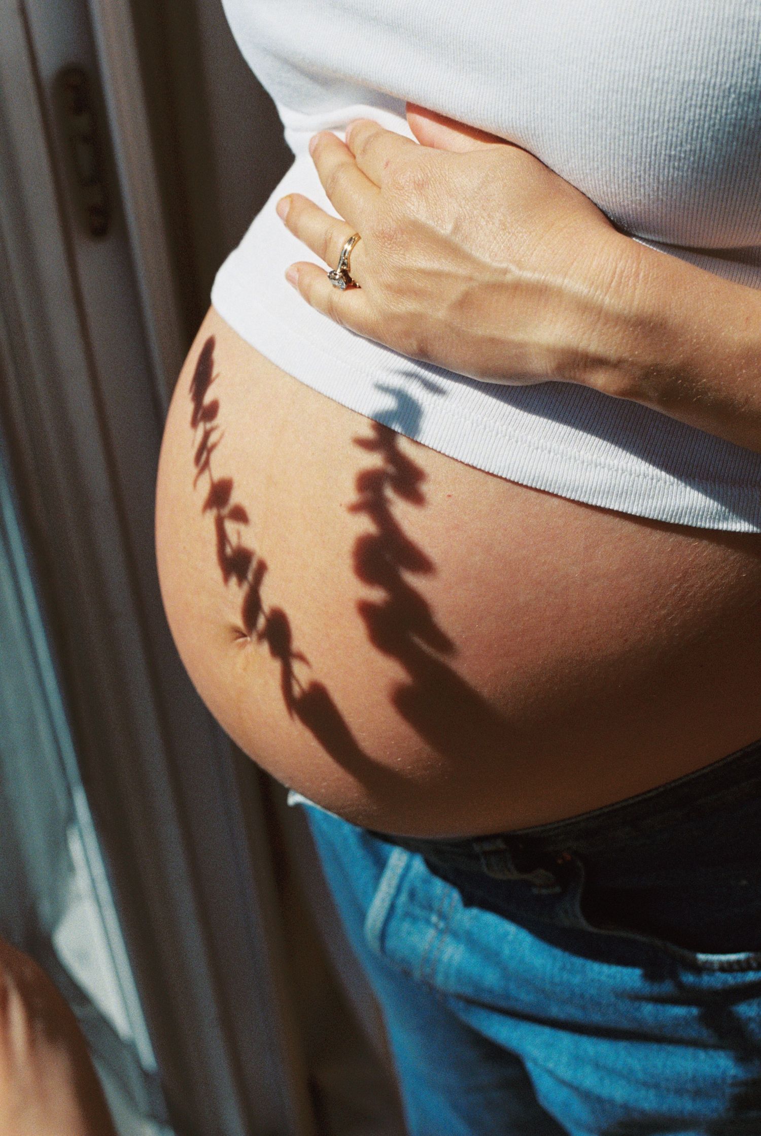 Pregnant woman in blue shirt and white lace shorts cradling her baby bump, smiling indoors.