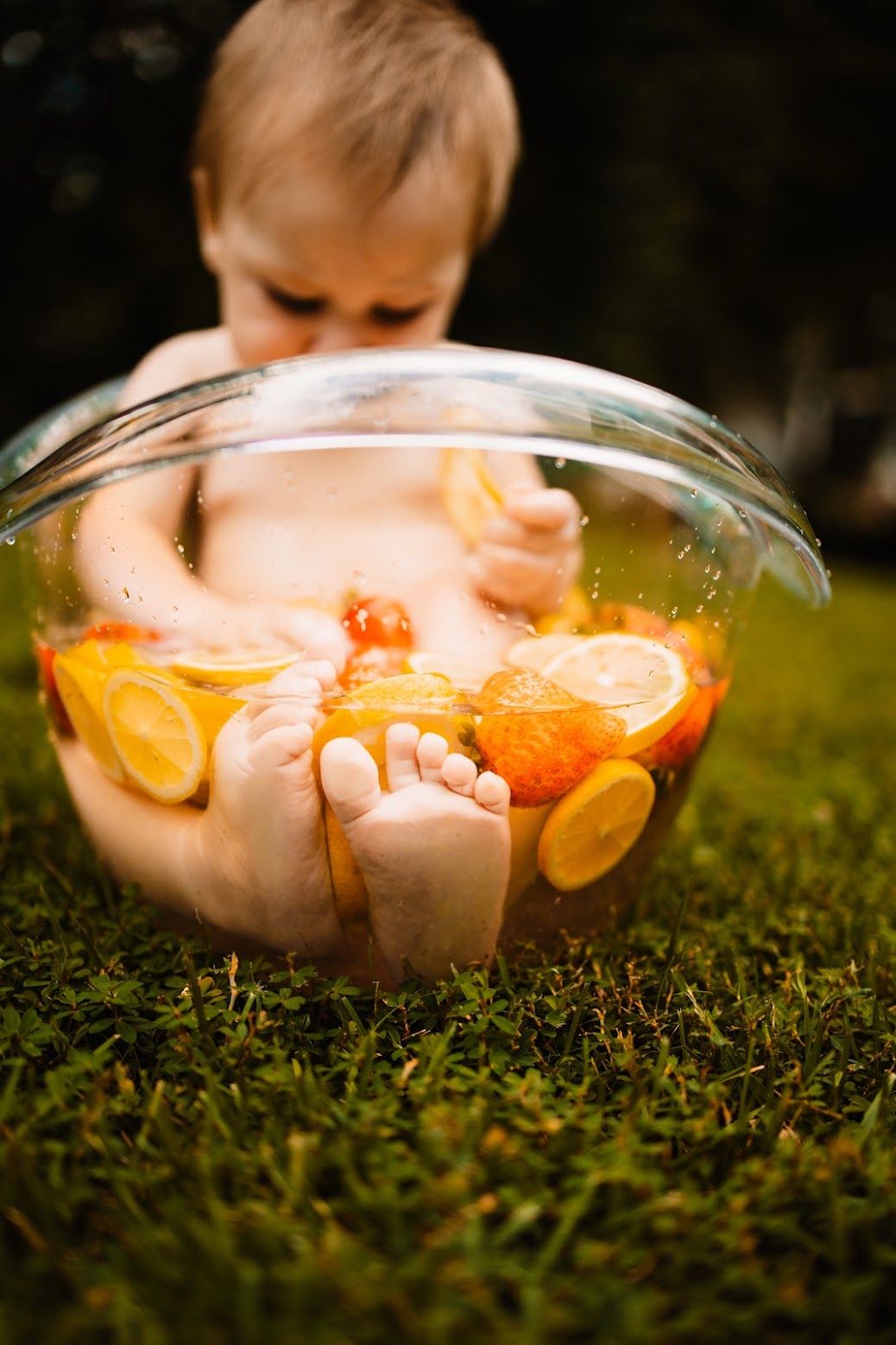 Baby feet peeking out of a glass bowl filled with water and citrus fruit slices on green grass in Oak Ridge, TN.