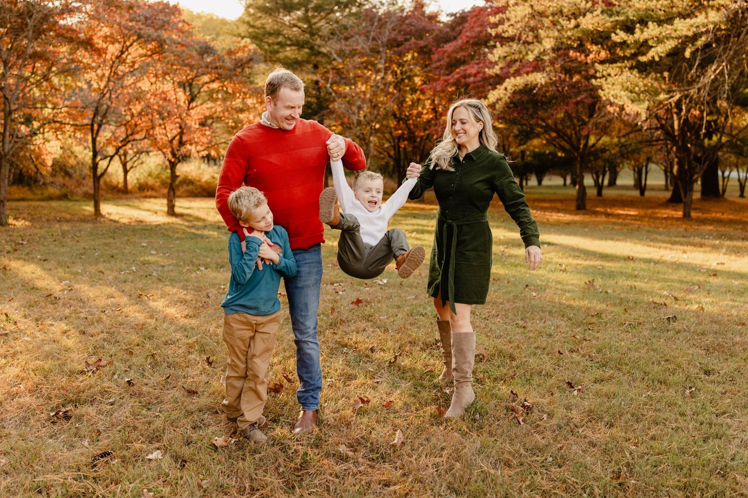 Family of four walking through a colorful autumn park, parents holding hands with young children among fall foliage.