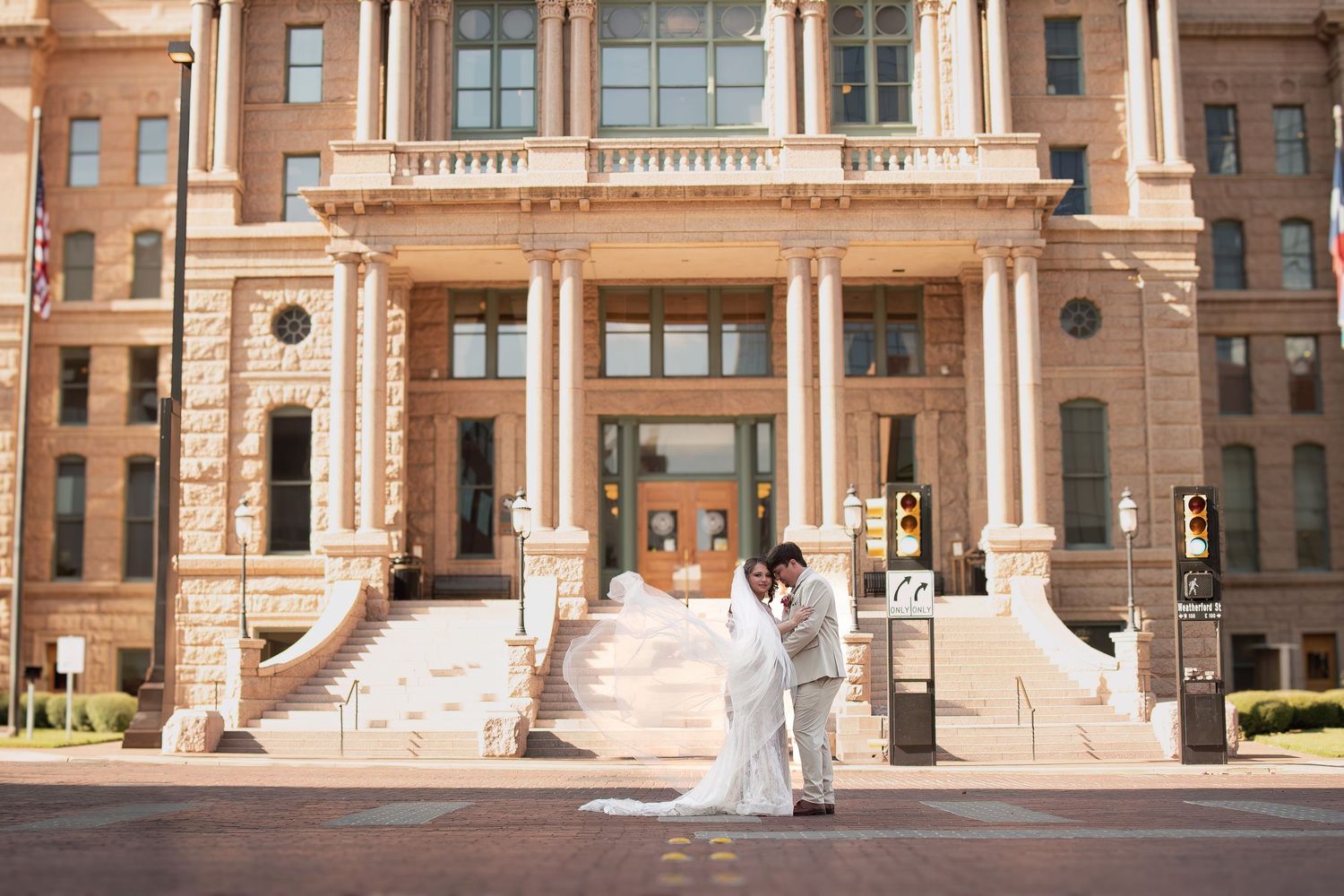 Bride and groom embracing in front of a grand historic building on their wedding day.
