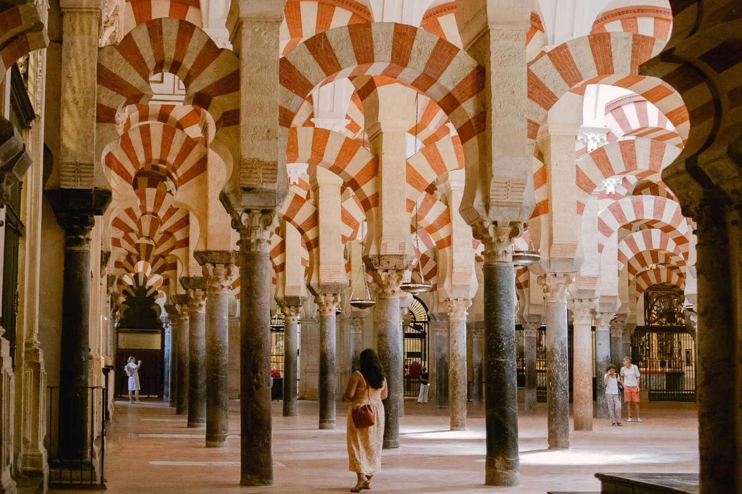 Tourist admiring stunning red and white striped arches inside the historic Mezquita Cathedral of Cordoba, Spain.