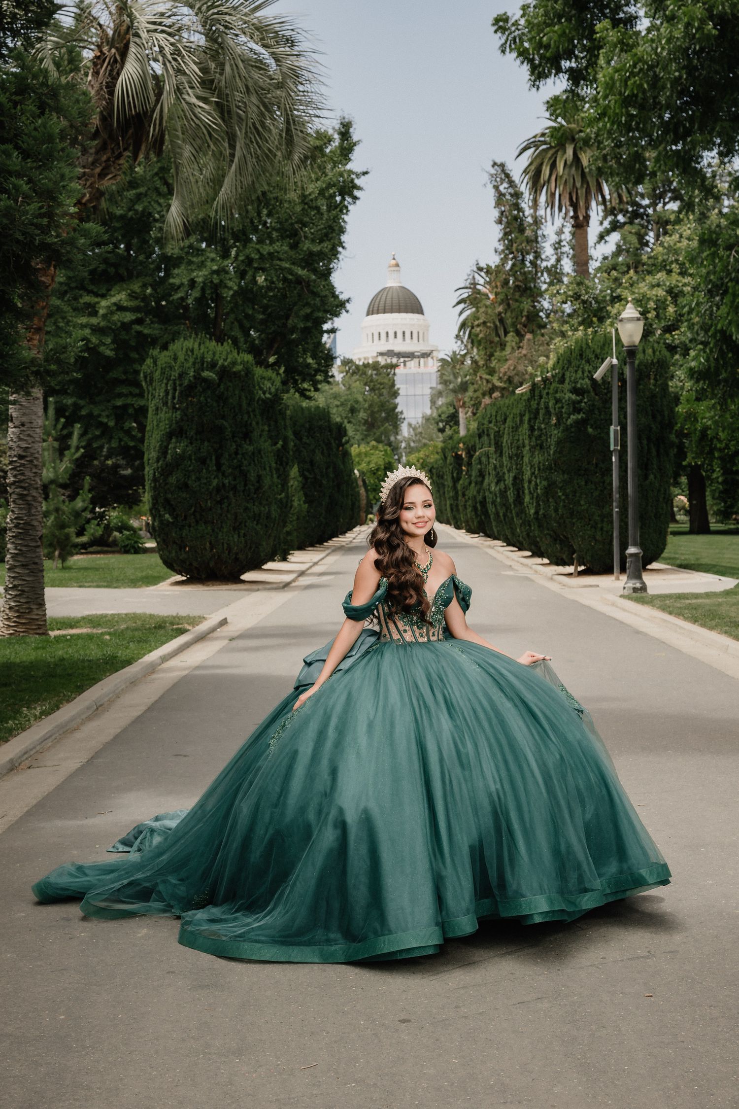 A light green dress flows elegantly on a tree-lined path with the State Capitol building visible in the background for Sacramento quince