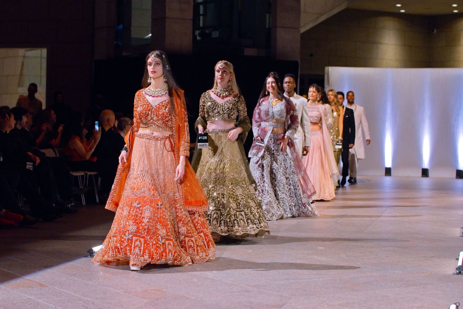 Models walk the runway in vibrant Indian bridal lehengas at a South Asian fashion show.