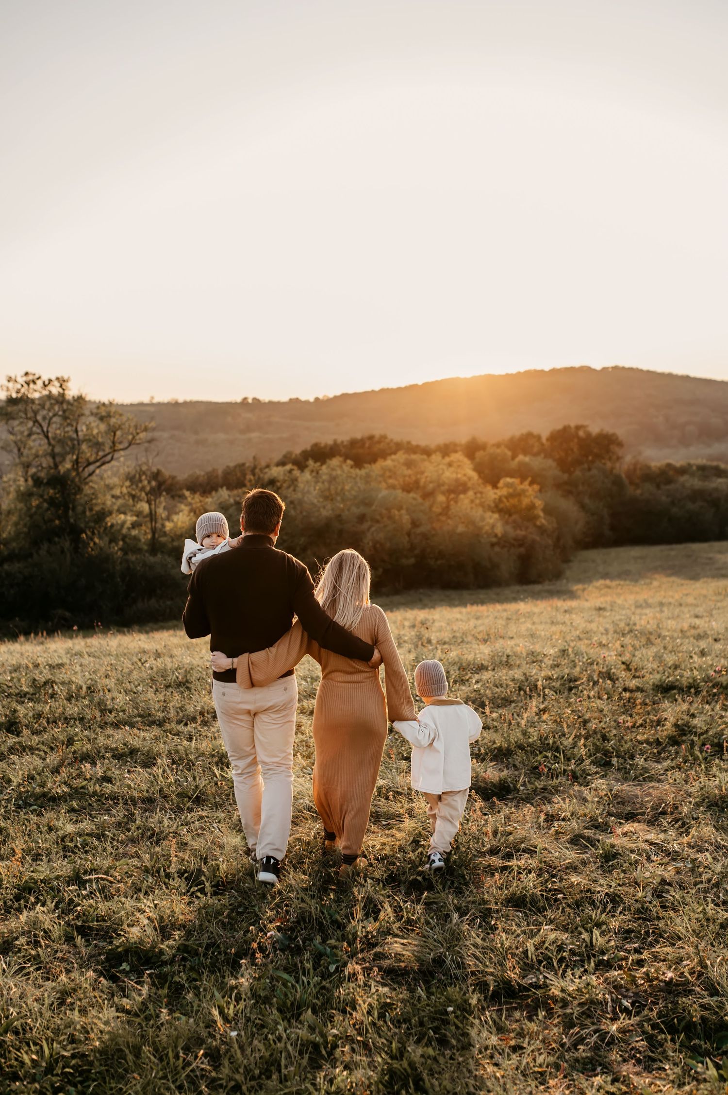 Family walking together in a golden sunlit meadow during sunset, creating silhouettes against the warm evening sky.