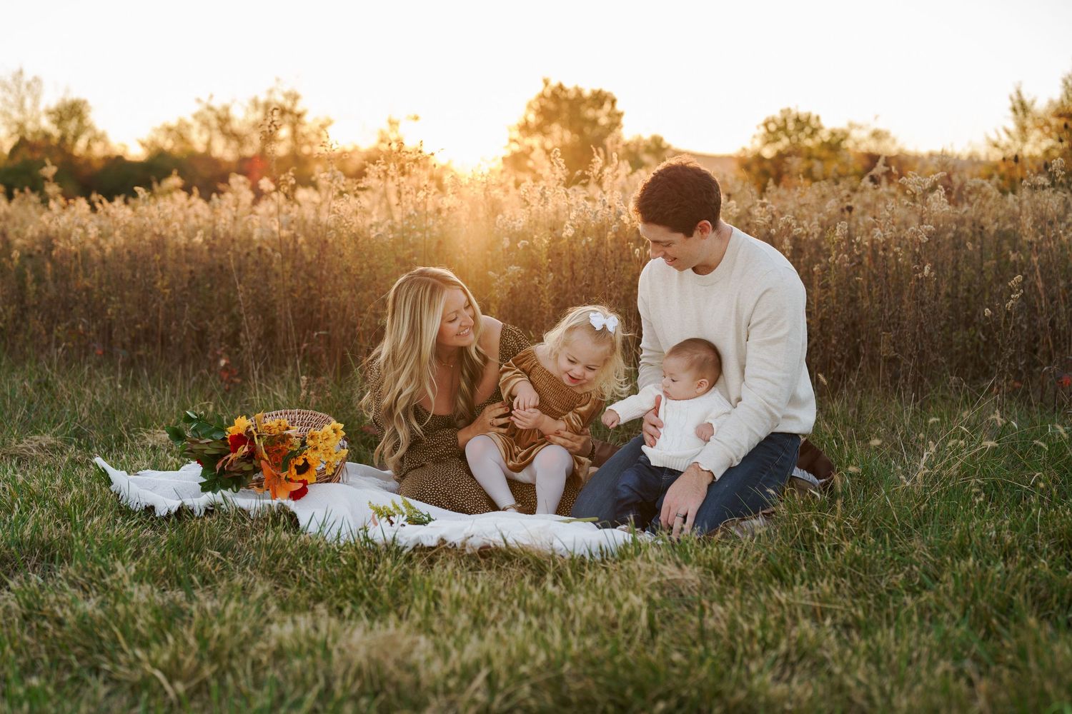 Family of four sitting on blanket in golden field at sunset with fall flowers, in Frederick, MD for a family session