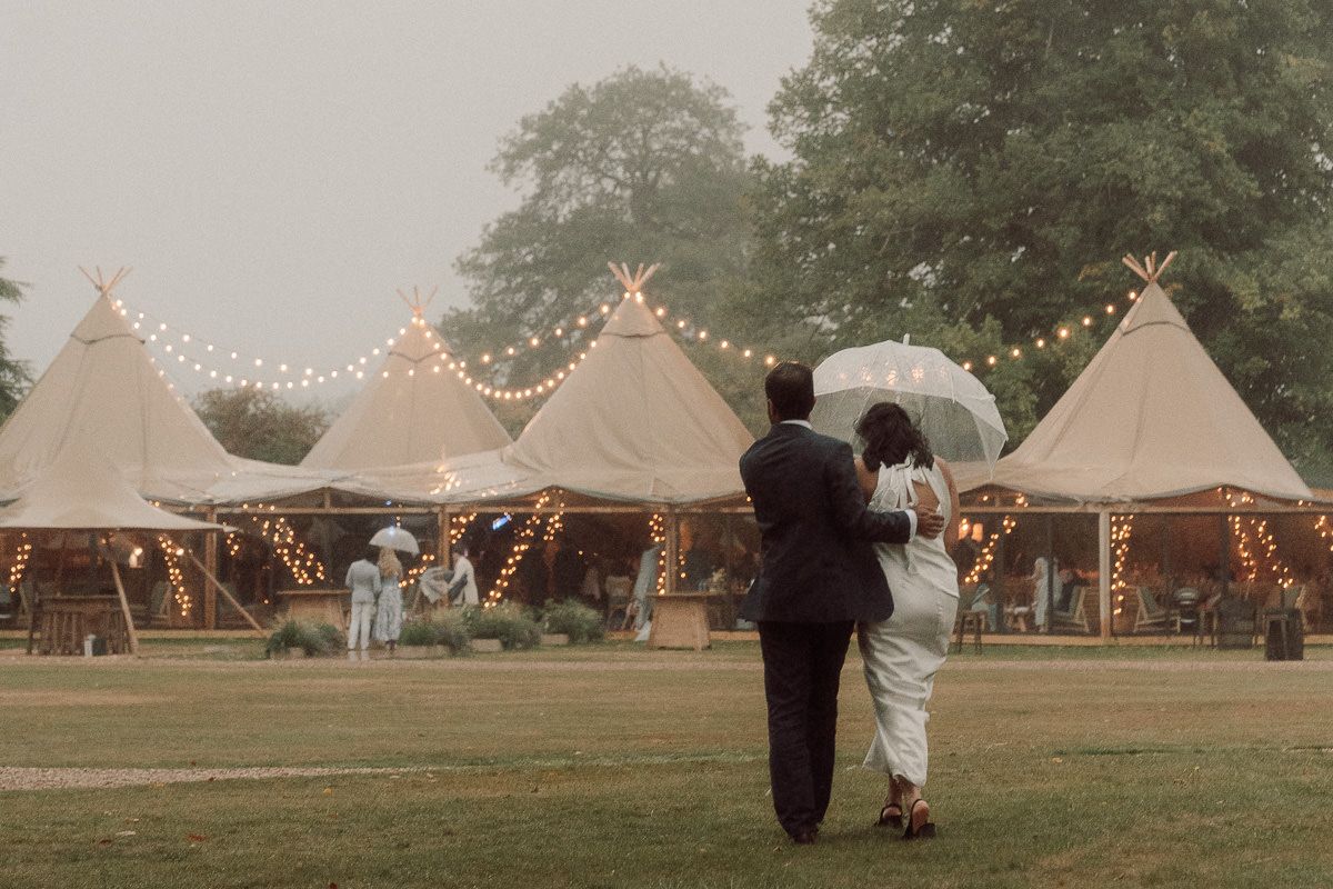 A romantic outdoor wedding reception setup with illuminated tipi tents and string lights creating a magical atmosphere at dusk.
