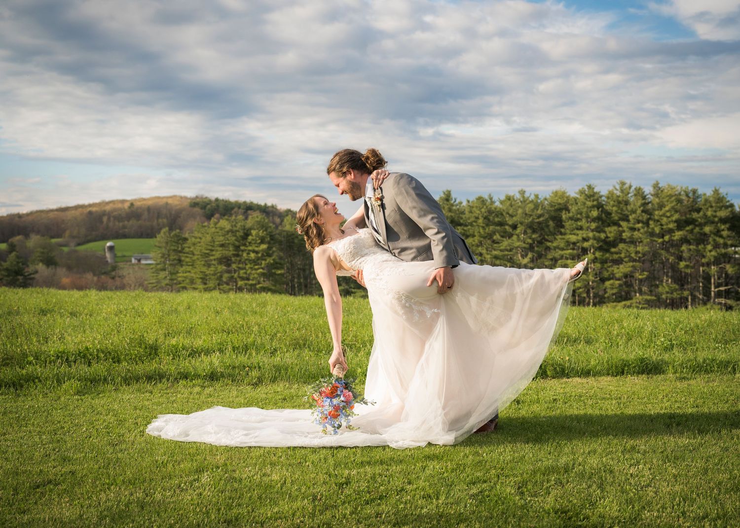Newlyweds share an intimate moment outdoors with autumn foliage and rustic architecture in background.