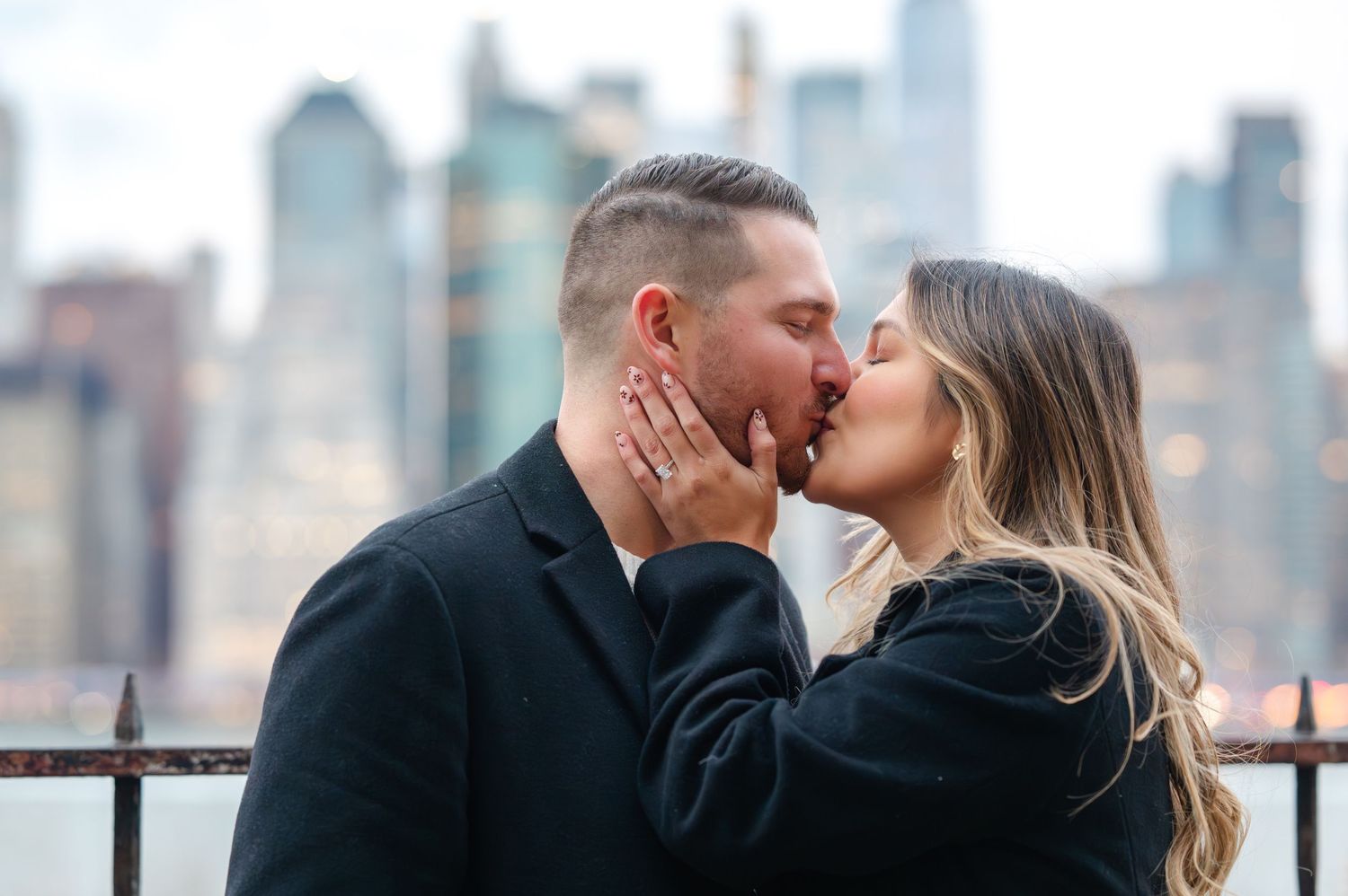 Couple sharing a romantic kiss with the New York City skyline in the background during an engagement photo session.