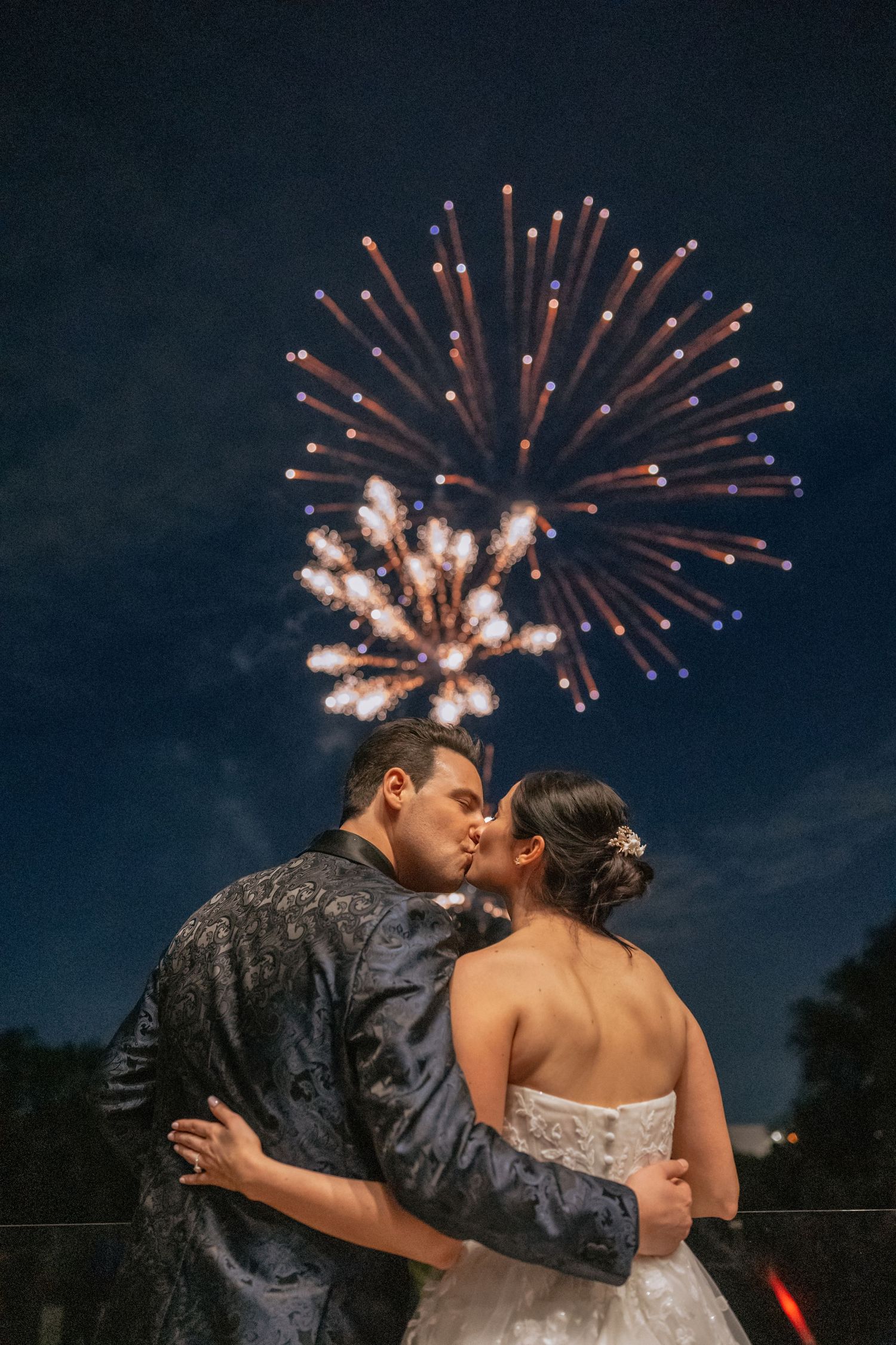 Couple posing in front of neon New Broadview Hotel sign on brick wall rooftop patio with string lights.