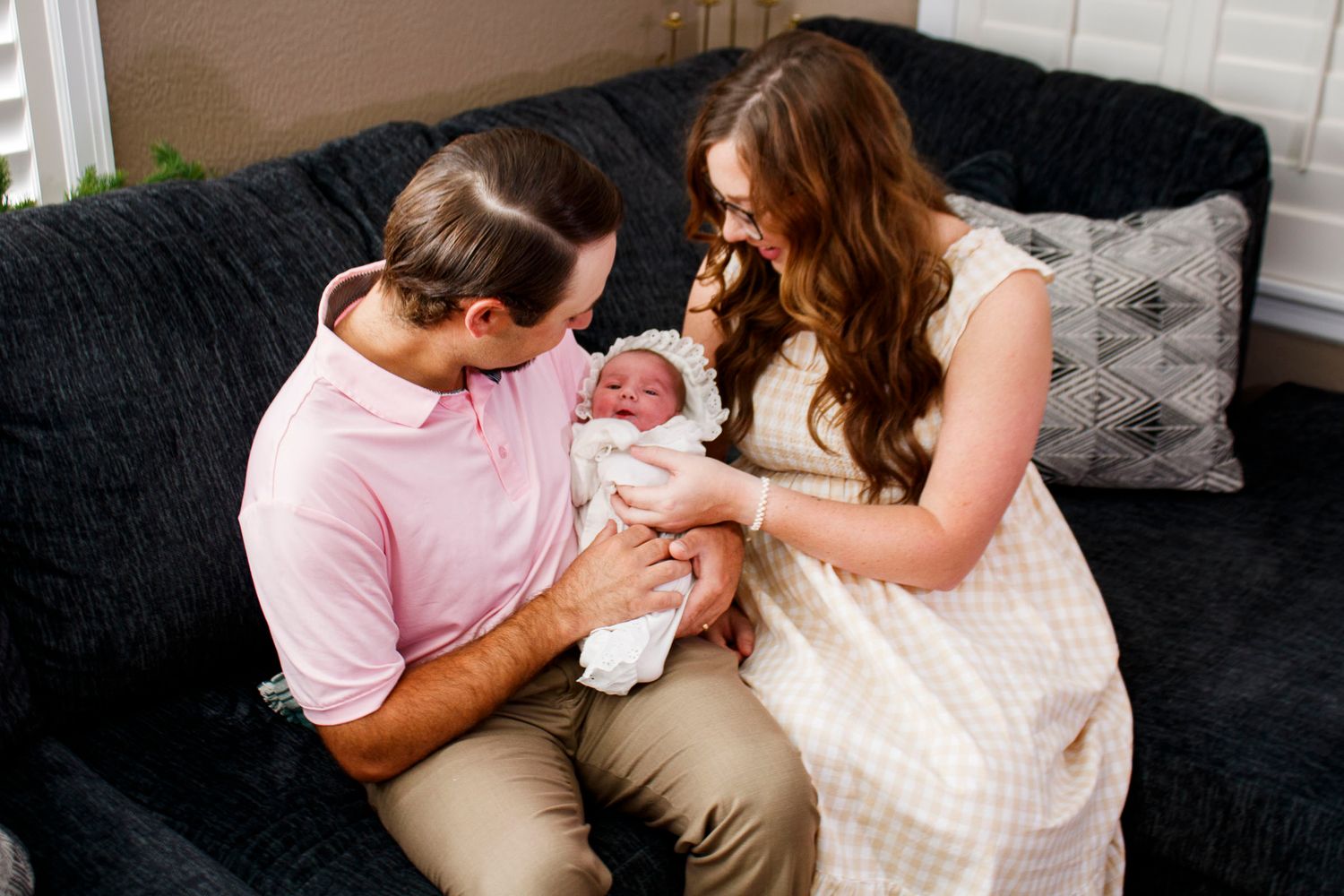 A couple in a cozy living room lovingly gazes at their newborn baby on a dark sofa for a newborn photo session in Spearman, Texas