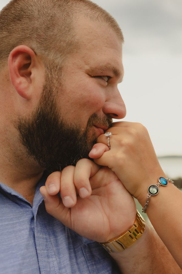 Bearded man kissing a woman's hand adorned with a diamond ring and turquoise bracelet in a romantic gesture.