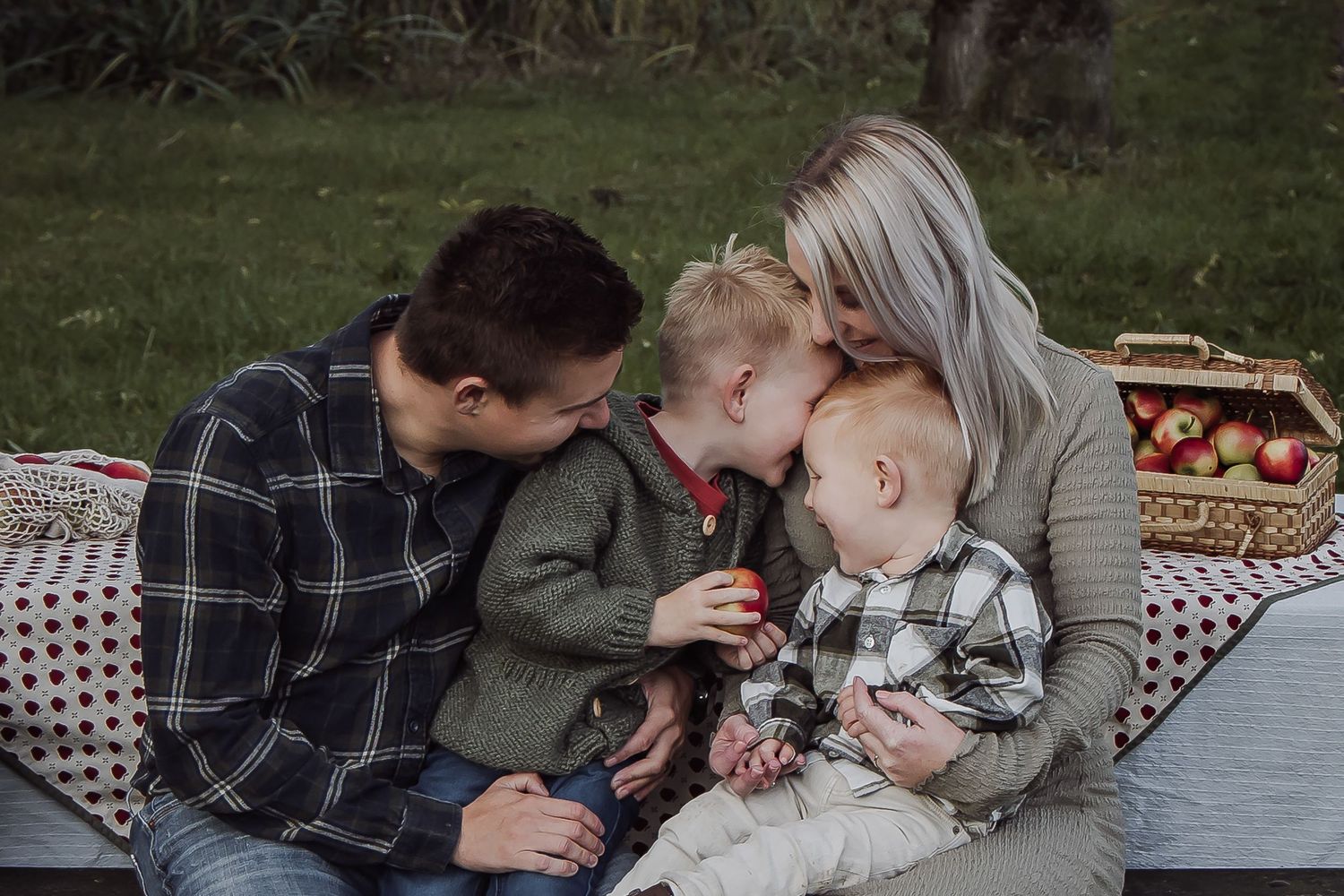A family laughing together, cuddling and snacking on apples during a relaxed outdoor family photoshoot in Woerden, Utrecht.