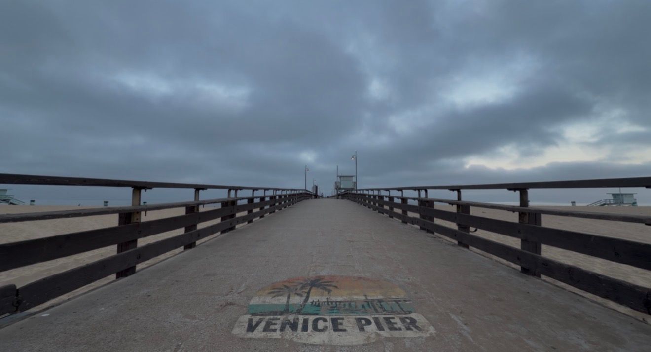 Venice Pier stretches into the overcast sky in Los Angeles, CA, with its iconic painted logo on the concrete walkway.