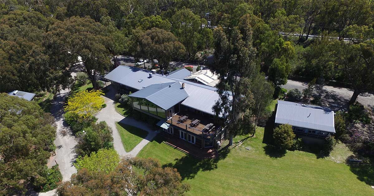 Aerial view of a charming rural property with multiple buildings surrounded by lush green trees and open lawns.