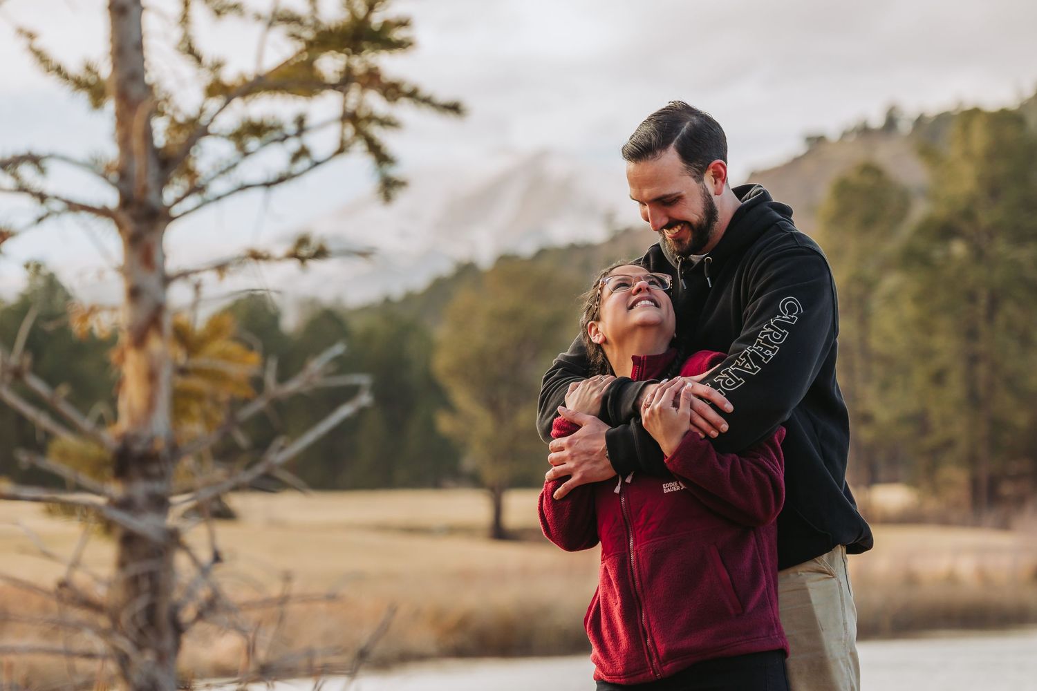 A couple in red and black attire shares intimate moments during a romantic outdoor photoshoot at sunset.