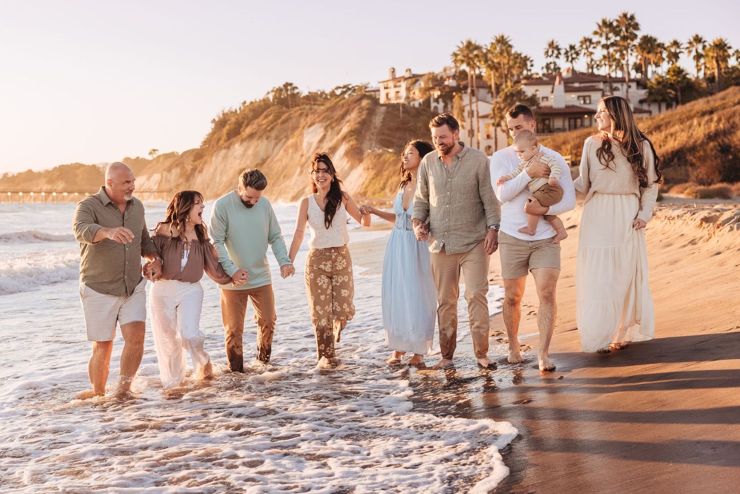 Family walking along a sunny beach at golden hour with ocean waves and coastal cliffs in the background.