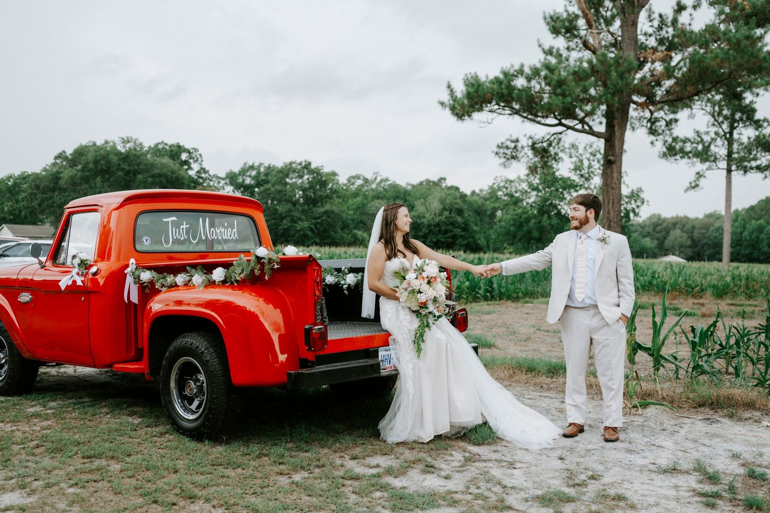 Bride and groom share a kiss in front of a vintage red Ford truck adorned with a Just Married sign on their wedding day.