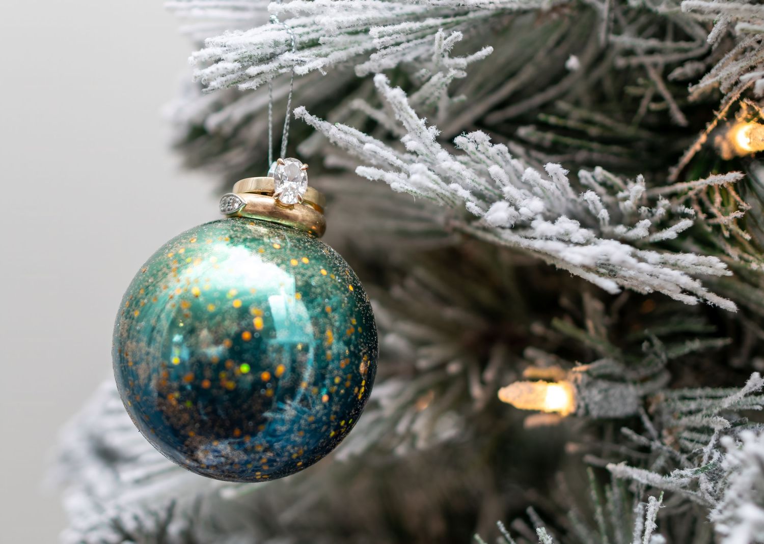 Close-up view of sparkly turquoise and silver glass ornaments hanging on a frosted Christmas tree branch.