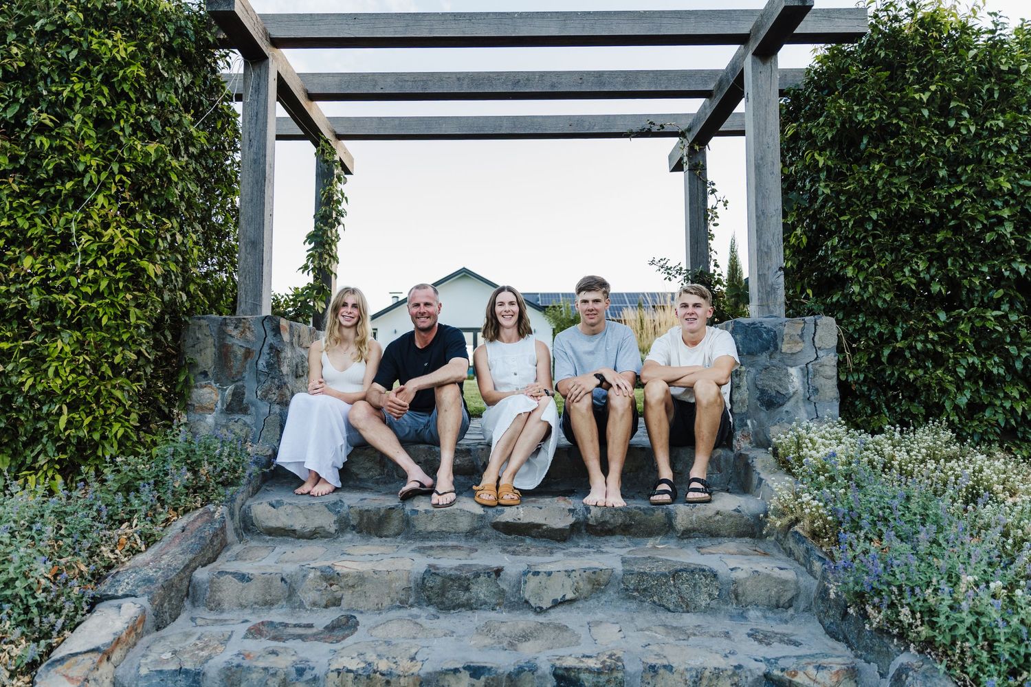 A casual group relaxing on stone steps under a modern pergola in a garden setting.