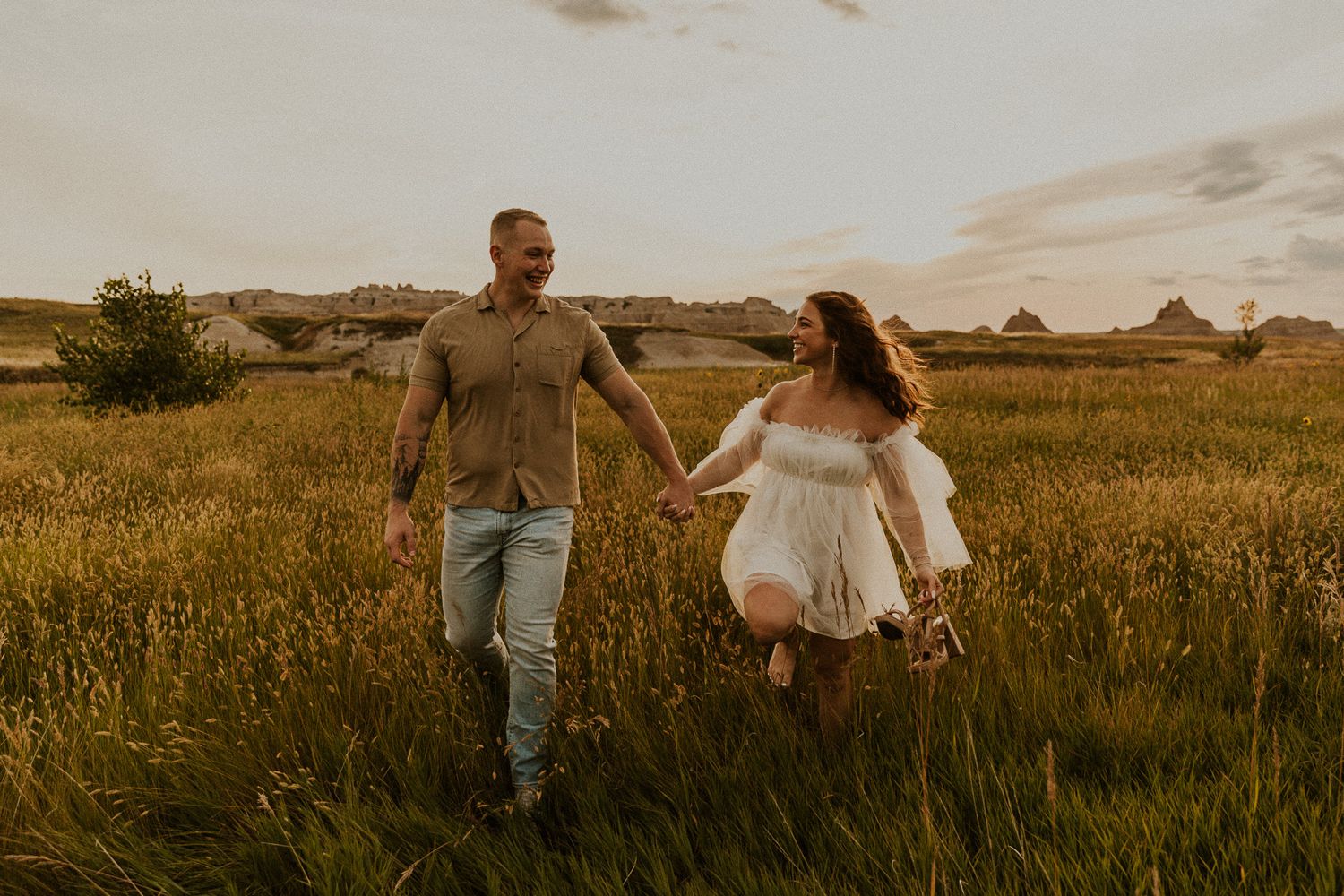 Couple running through field at sunset during Badlands National Park engagement session.
