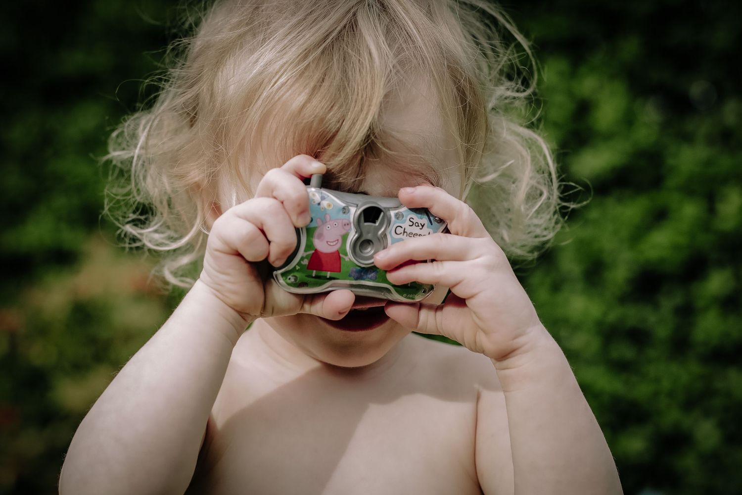 Small hands hold up a vintage camera against a green outdoor background.