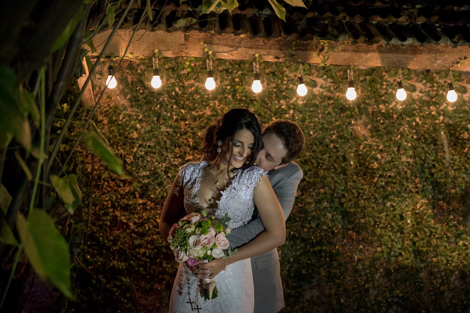 A couple shares a tender moment under string lights in a garden setting.