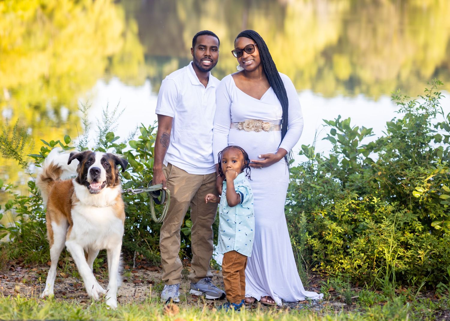 Family with dog poses for maternity photo in front of yellow autumn foliage.