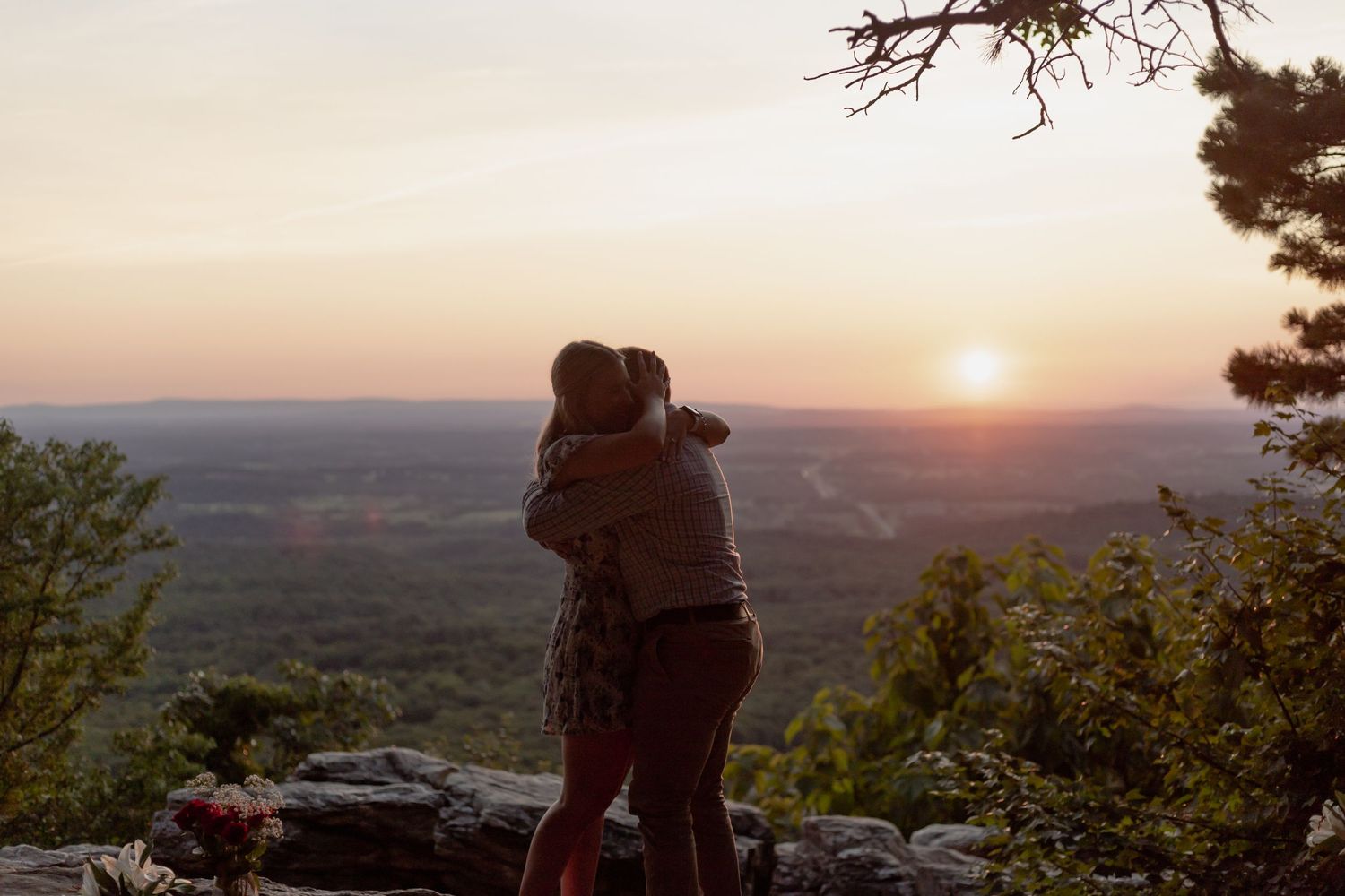 Silhouetted couple embracing while watching sunset from a scenic mountain overlook.