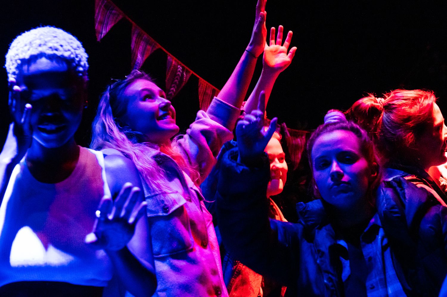 A crowd dances under colorful nightclub lights at a party celebration.