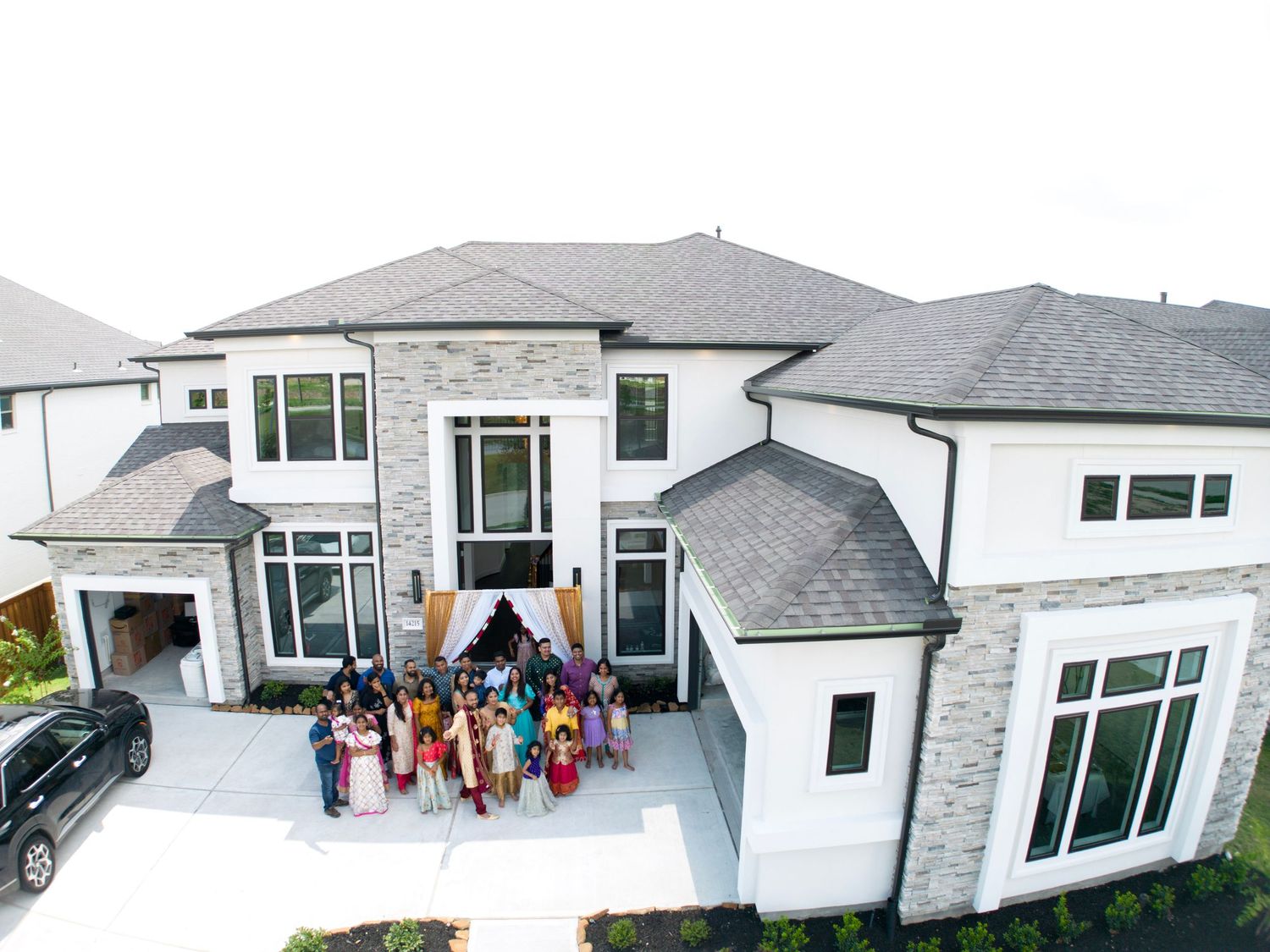 Large modern white house with multiple guests gathered at the entrance for a celebration.