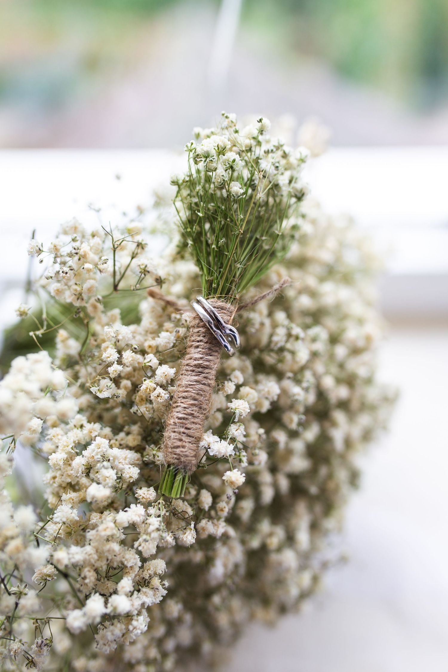 Close-up of baby's breath bouquet wrapped in rustic twine against blurred background.