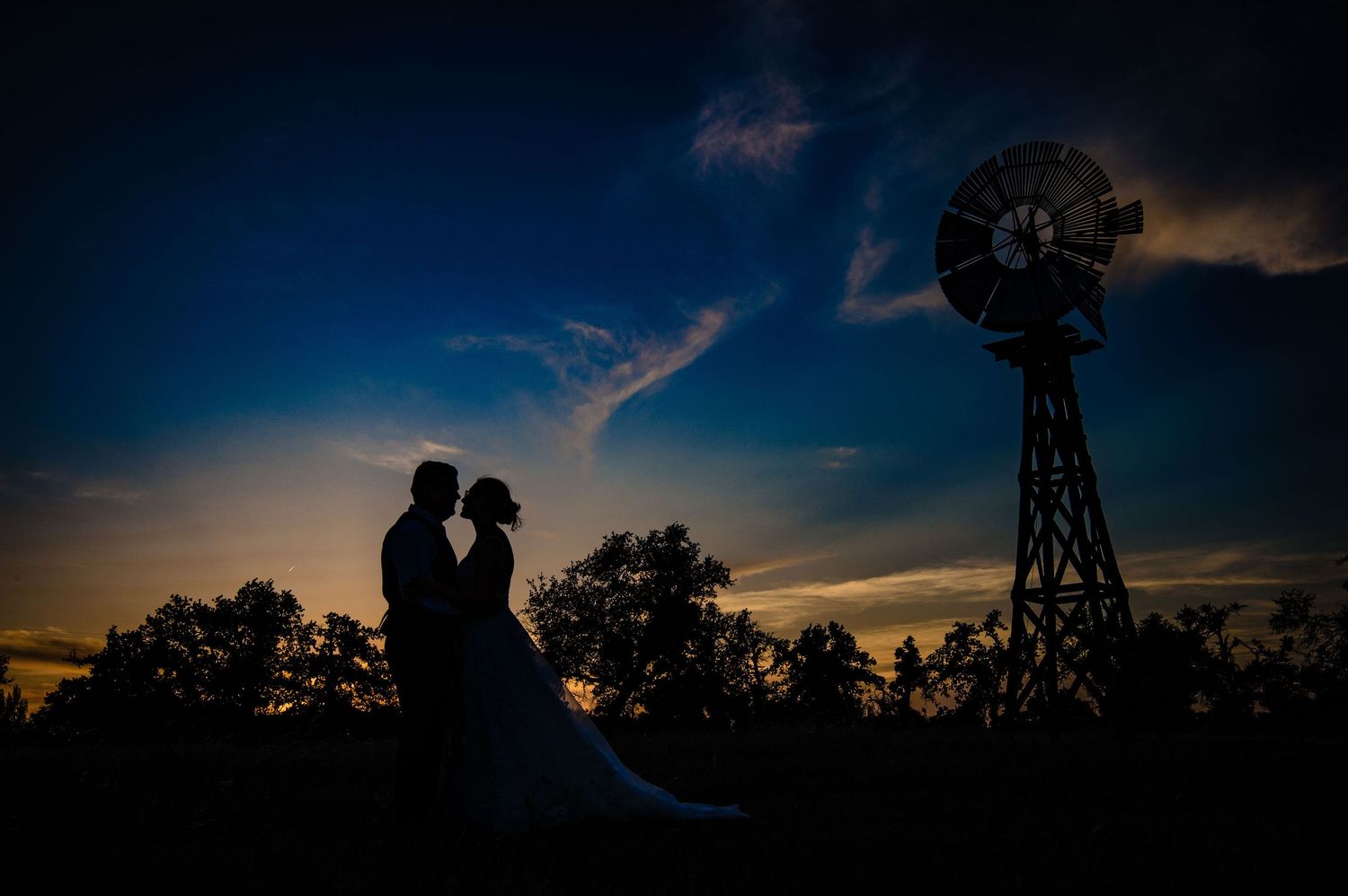 Wedding couple silhouetted against dark blue sky with vintage windmill.