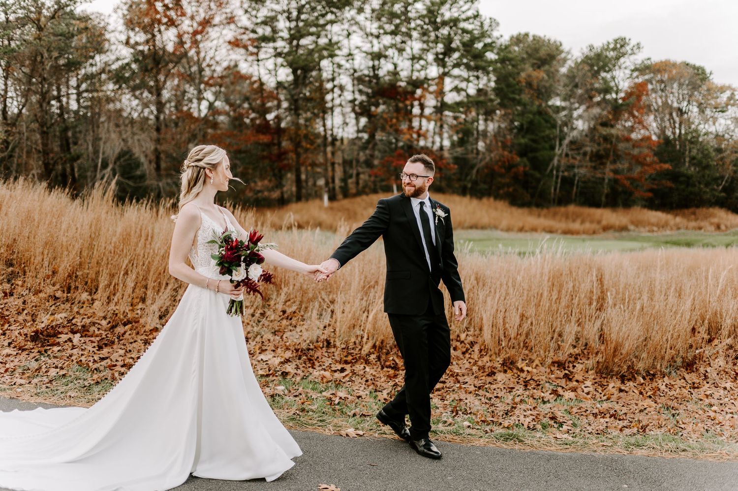 Wedding couple walks through tall autumn grass during their outdoor photo session.