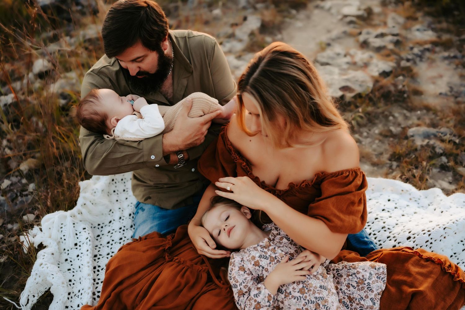 Intimate family moment captured on a white lace blanket during an outdoor photo session.