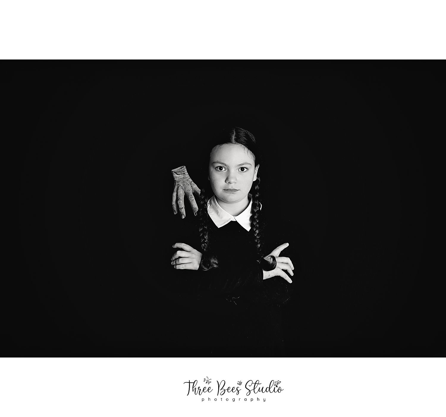Dark dramatic portrait against black background with gothic styling and posed hands.