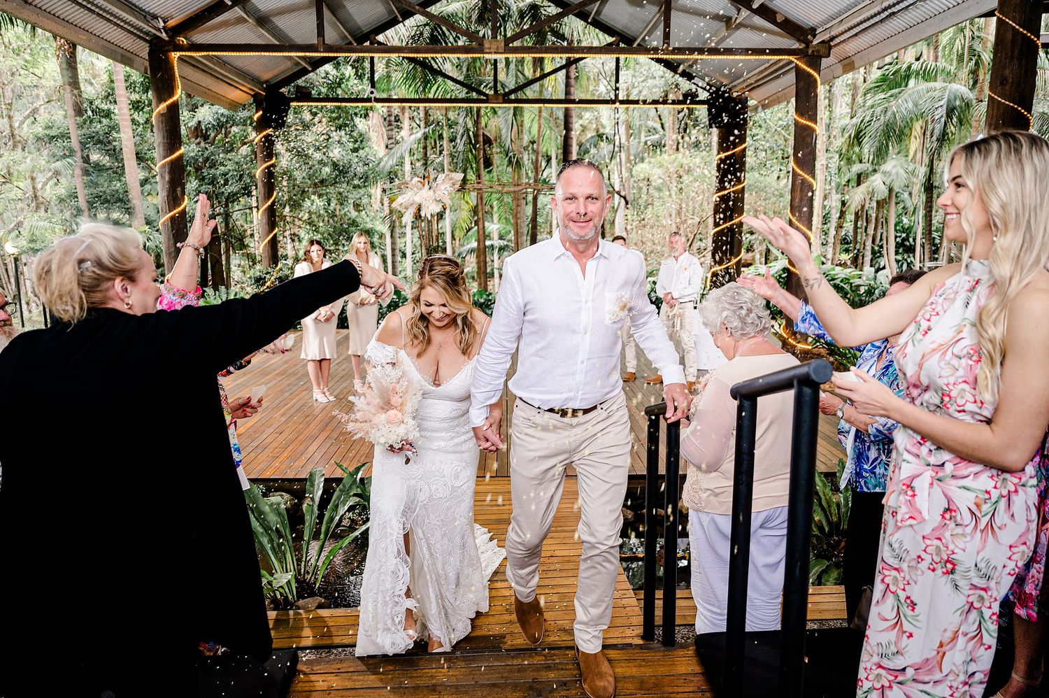 Wedding celebration under wooden pavilion with guests raising hands in celebration.