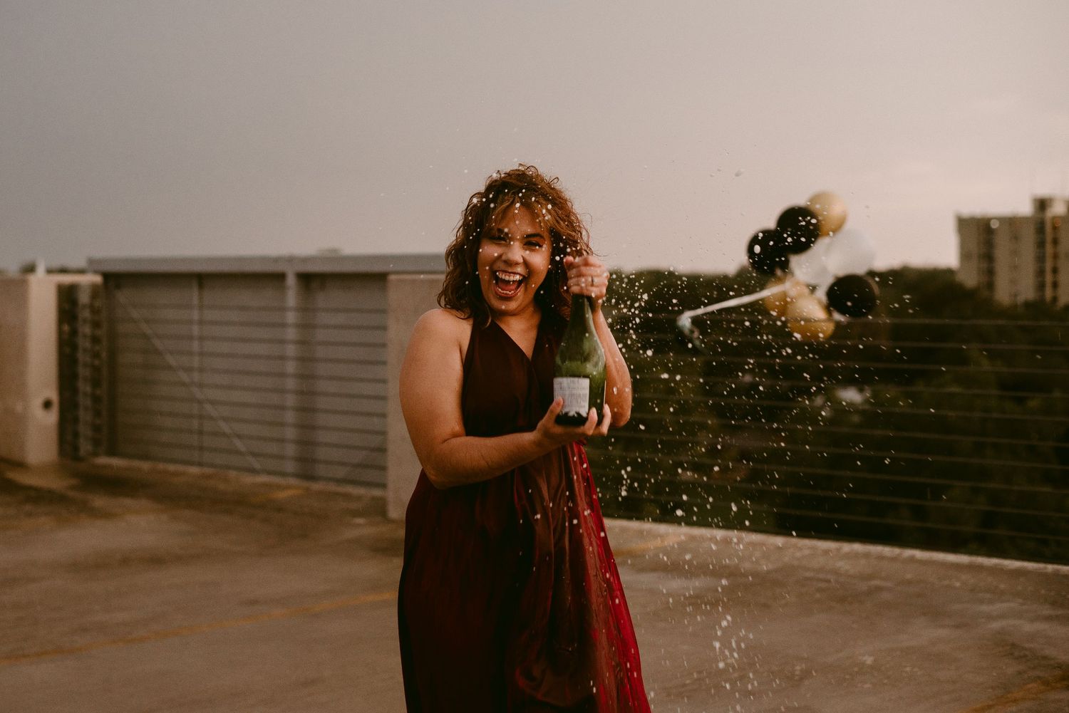 Joyful rooftop celebration with champagne spray at sunset.