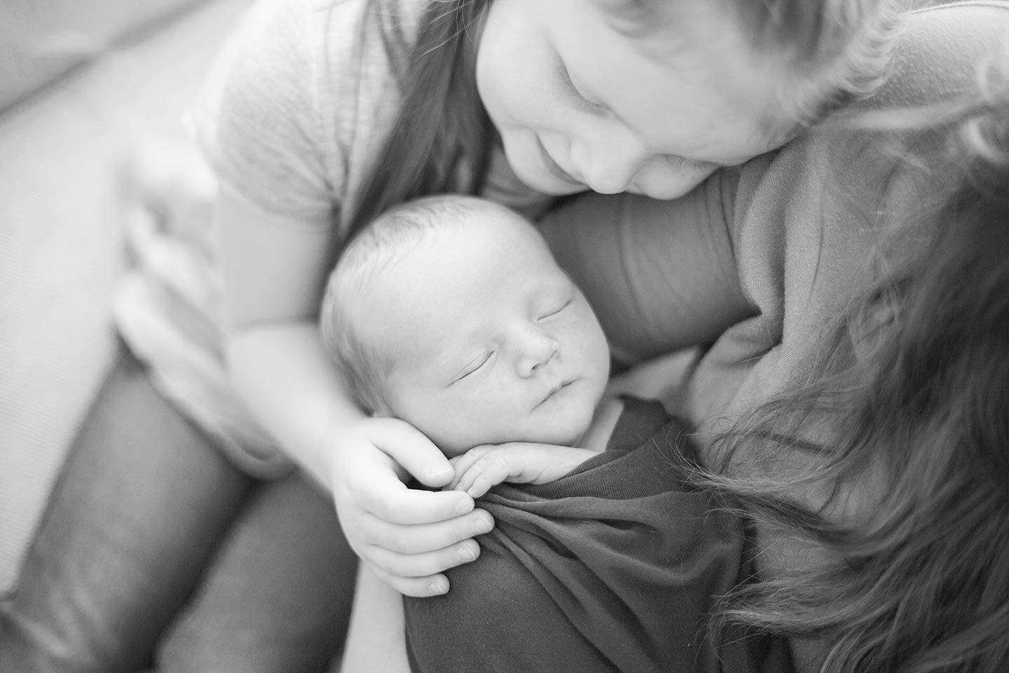 mother holding newborn baby while sister snuggles in and looks at her baby brother