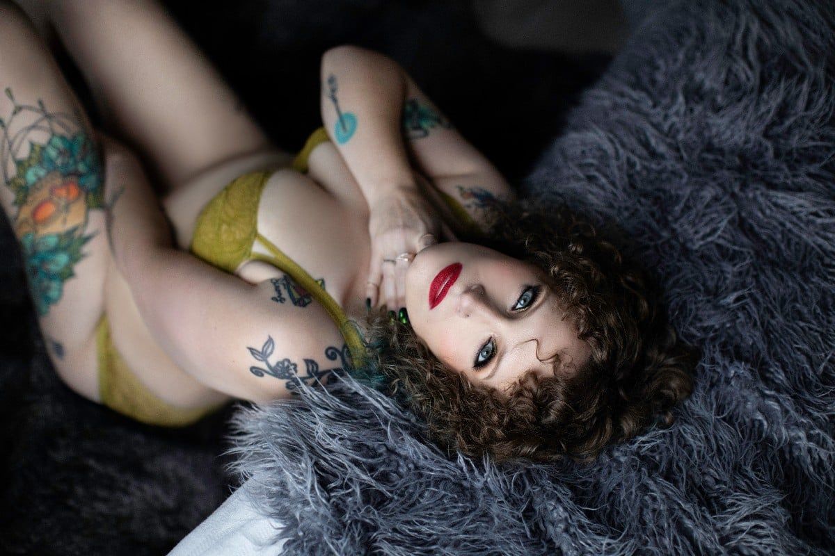 Artistic boudoir portrait on grey faux fur with colorful tattoos and yellow lingerie.