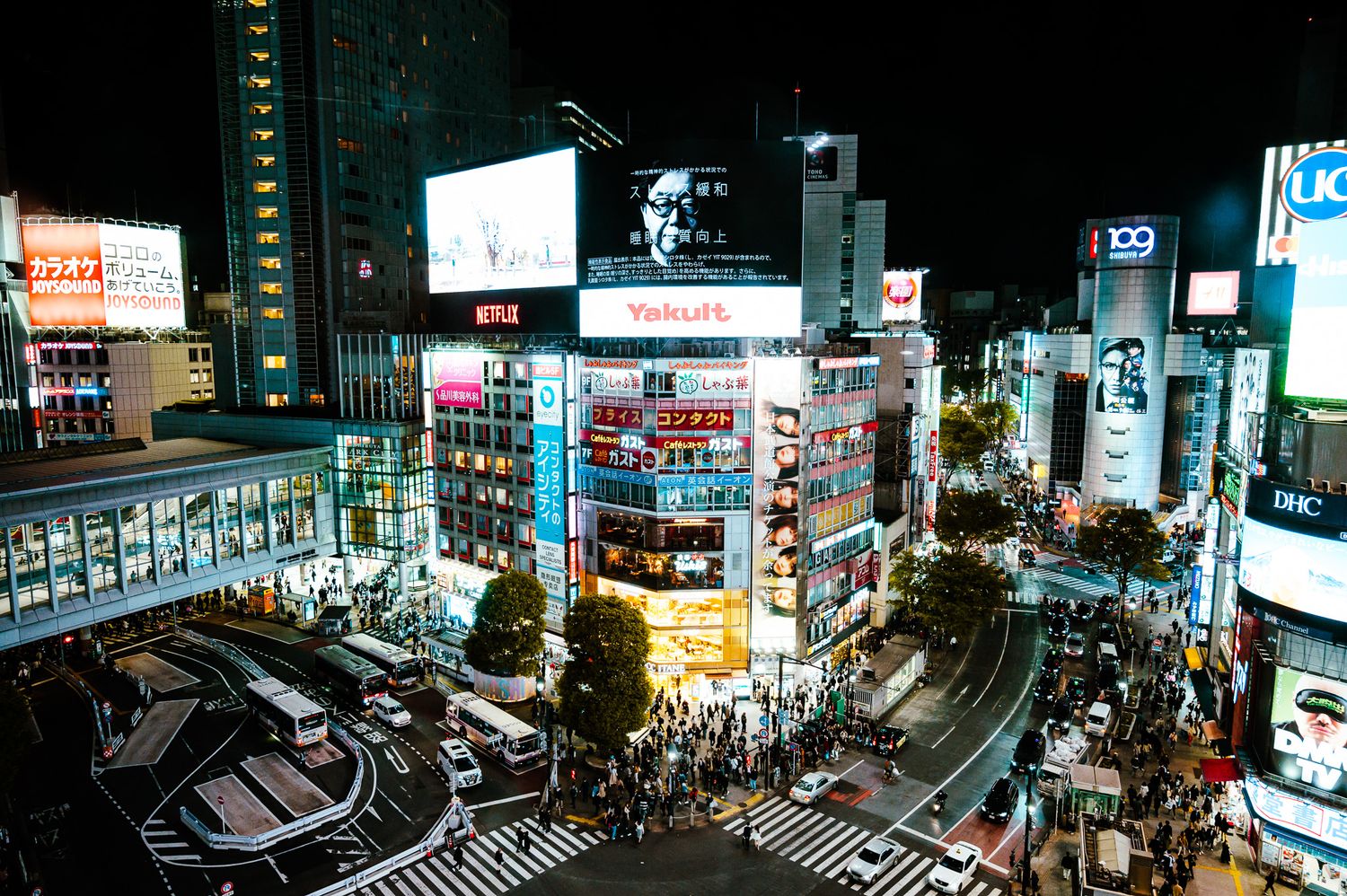 Vibrant nighttime cityscape of Shibuya crossing with illuminated billboards and traffic.