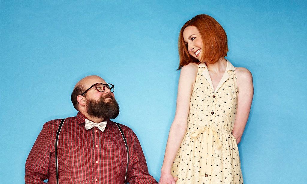 Whimsical studio portrait of couple in contrasting outfits against bright blue background.