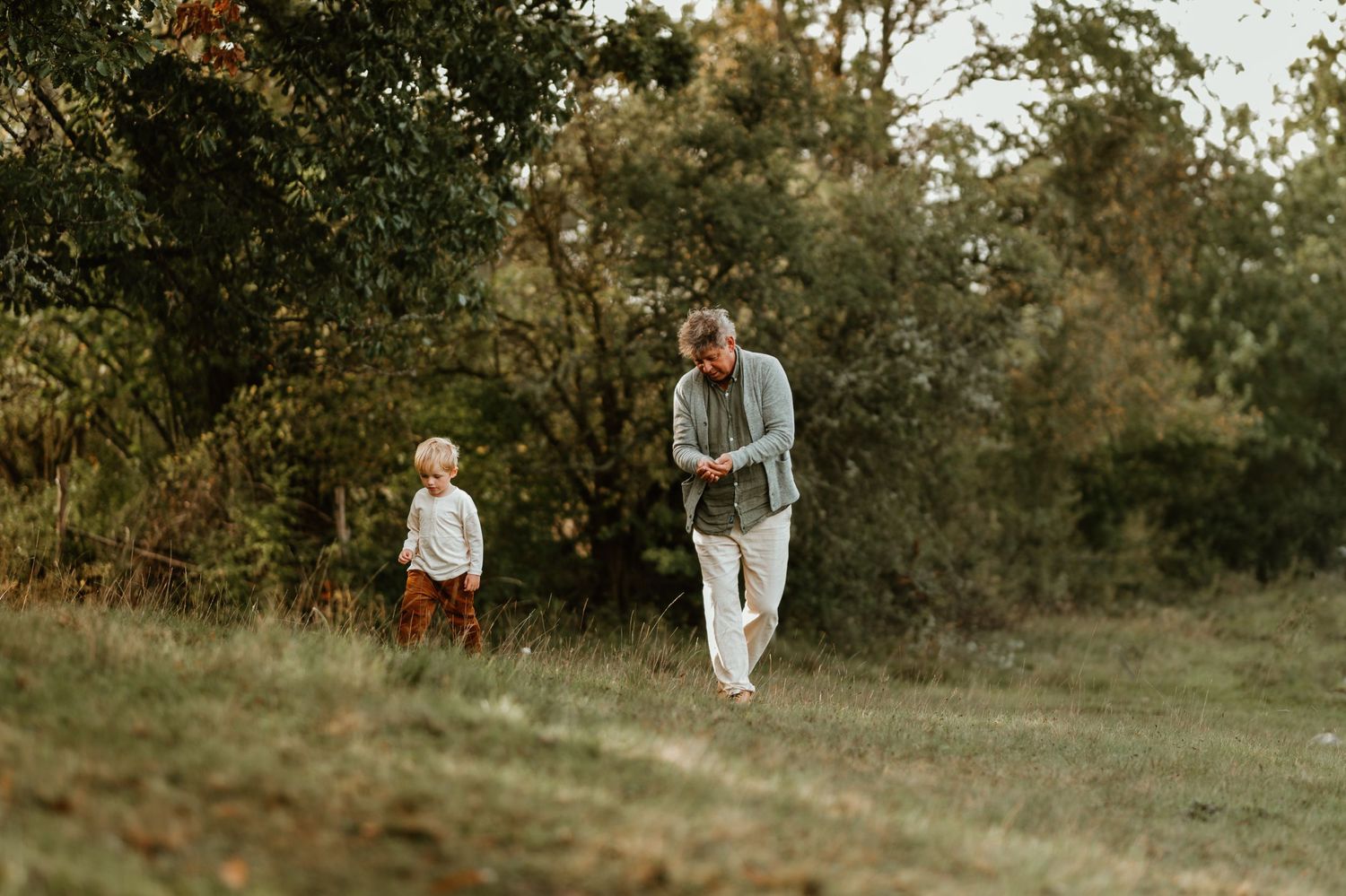 Two figures walk along a grassy hillside during golden hour in autumn.