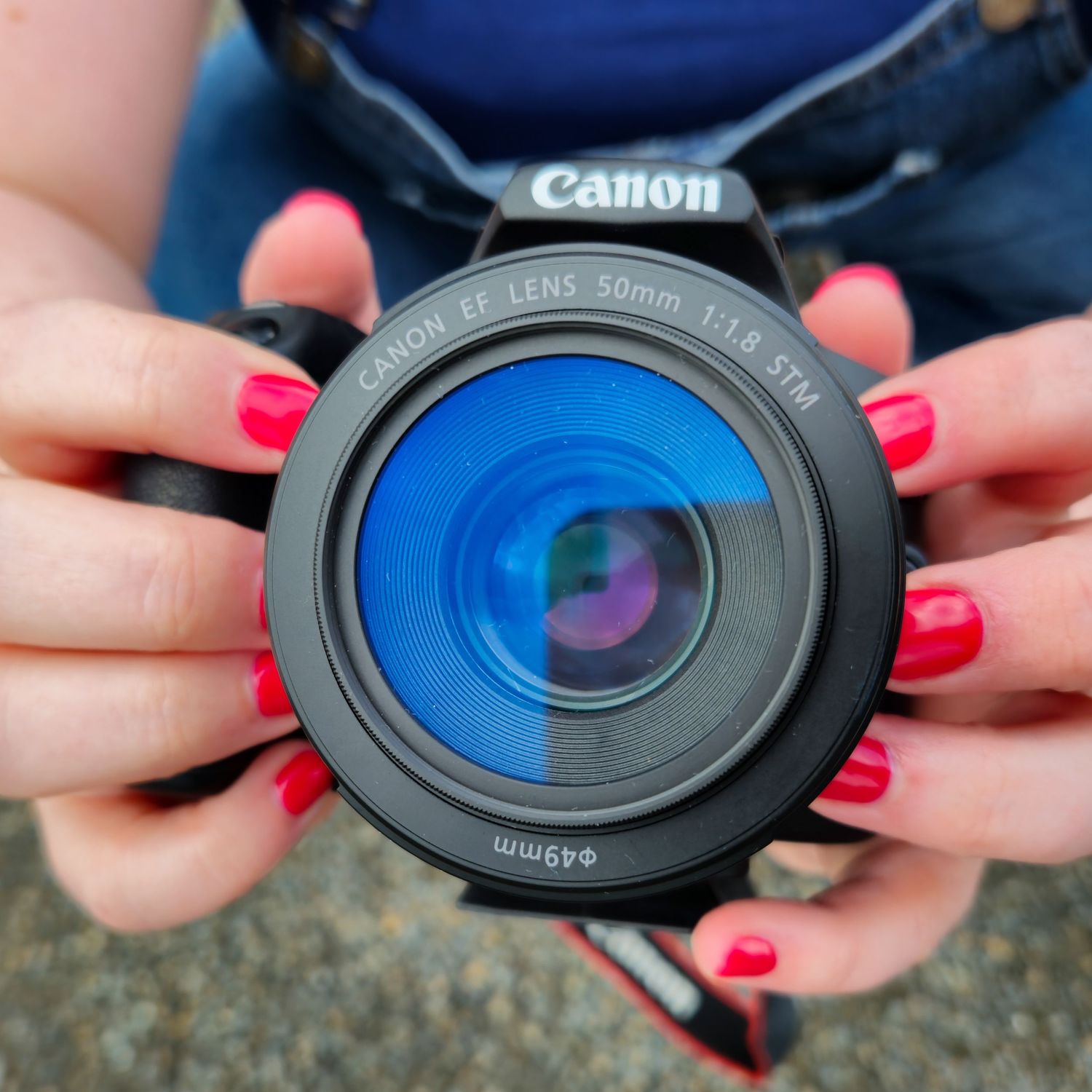 Close-up of hands with red nail polish holding a Canon camera lens.