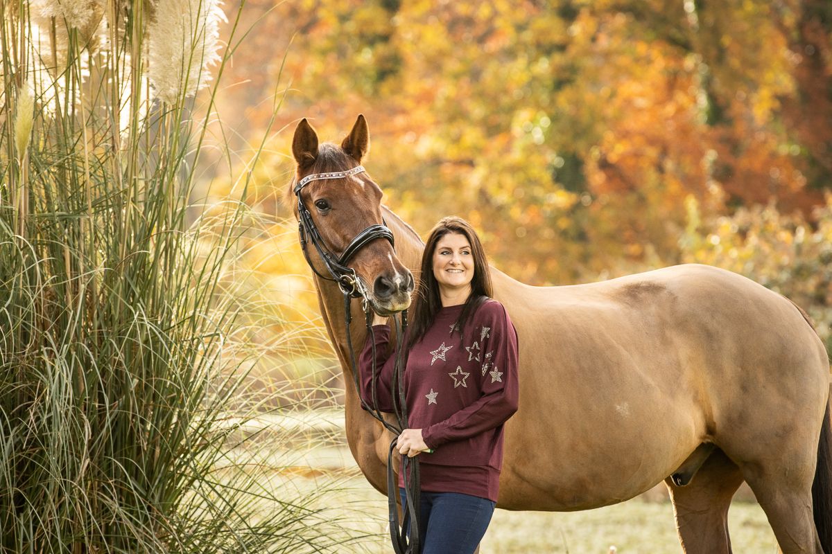 A dun colored horse poses with companion during golden autumn photoshoot near tall grasses.