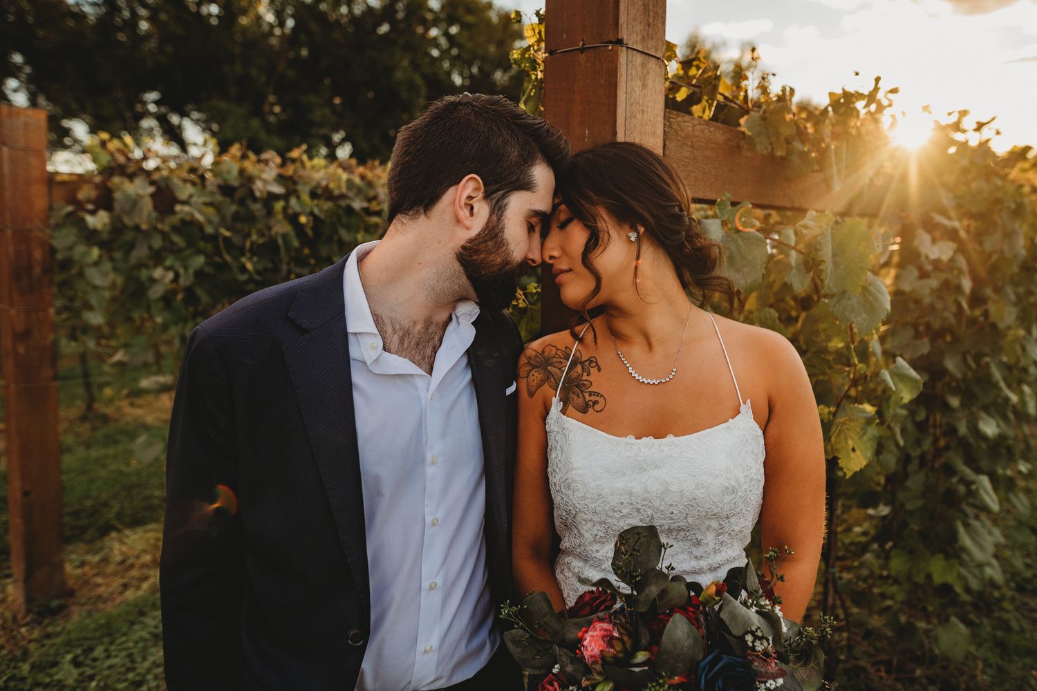 A couple shares an intimate moment among vineyard rows at golden hour.