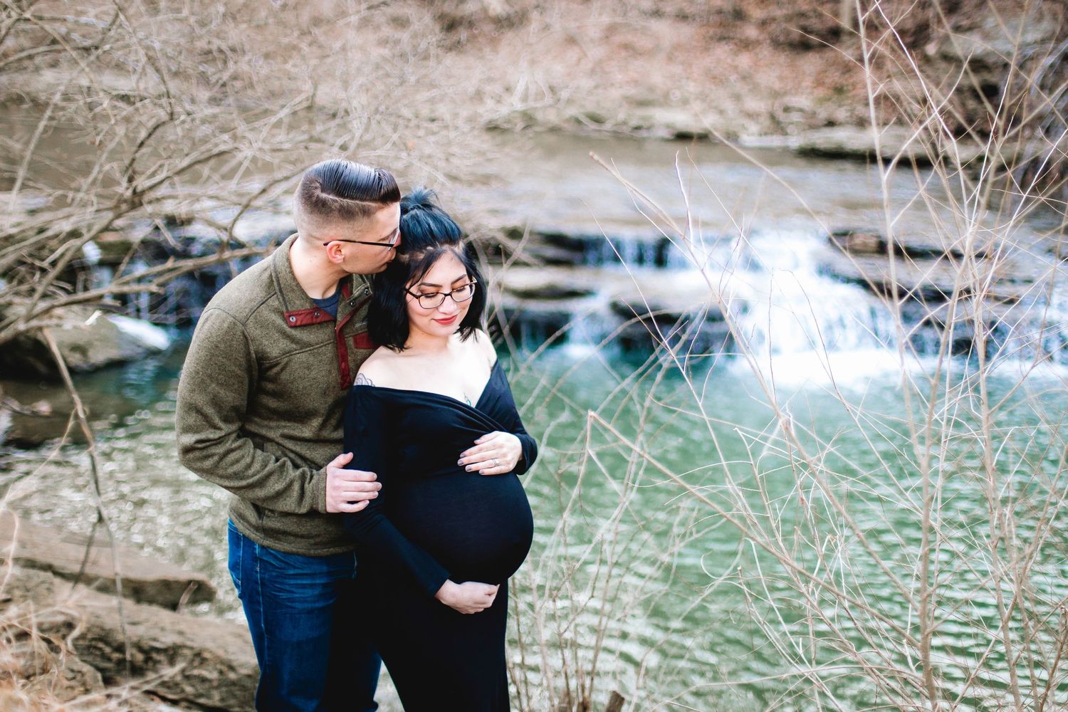 man and pregnant woman posing for maternity photo shoot near a river in Kansas City, Missouri