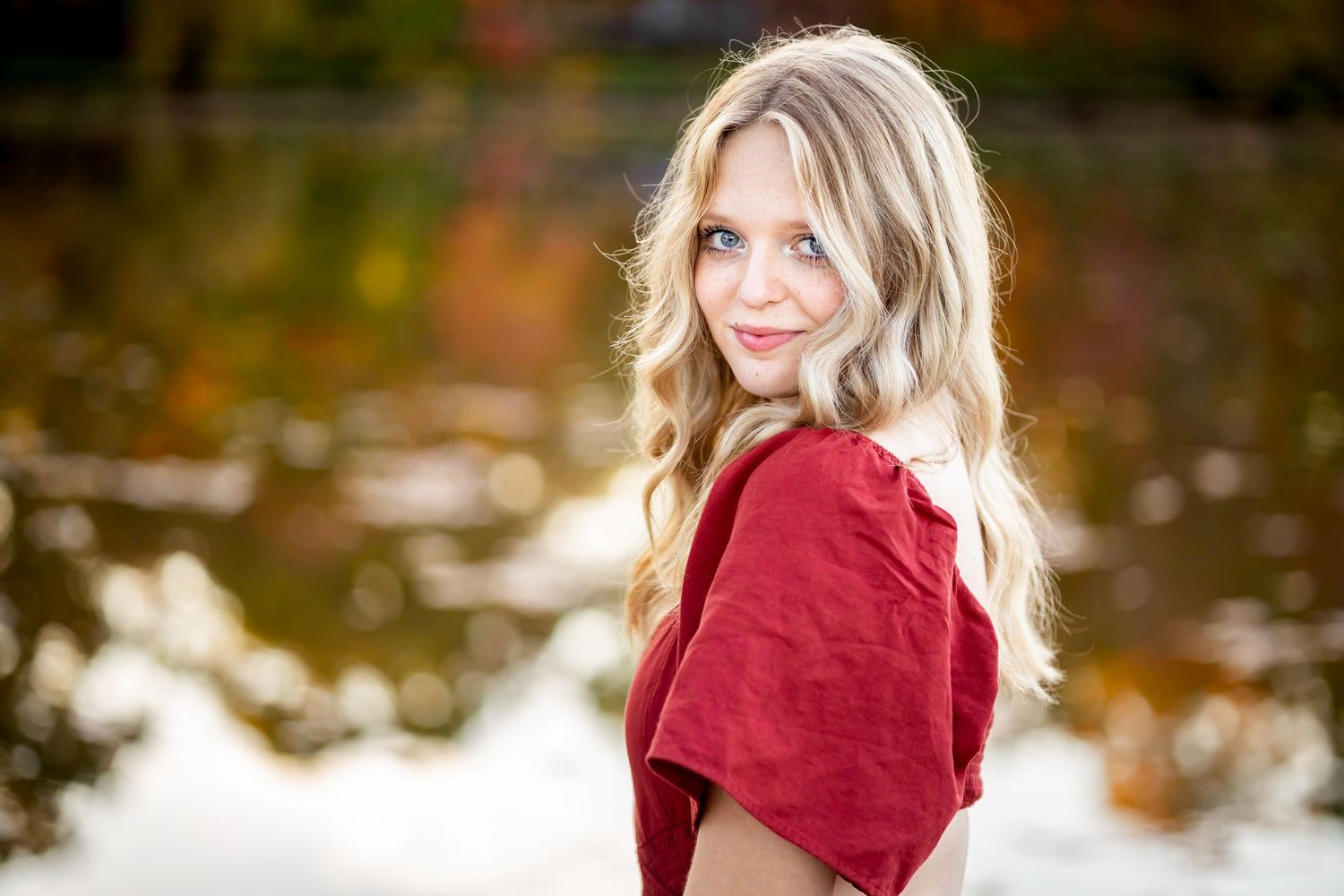 Portrait of woman in red top by reflective pond in autumn.